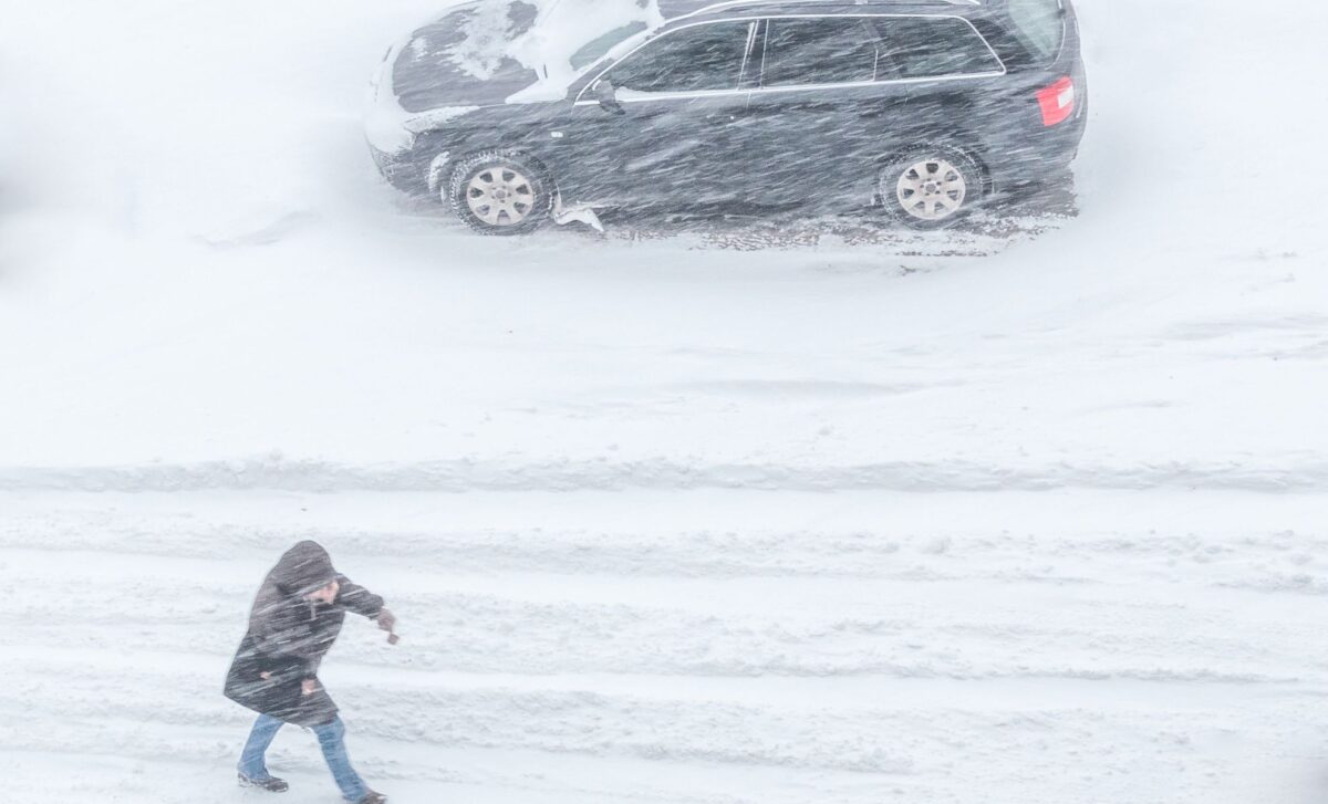 Un homme qui marche et une voiture qui roule dans une tempête de neige pour évoquer la Météo du moment