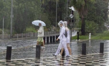 Des personnes avec des parapluies traversant une route mouillée pour illustrer une météo agitée