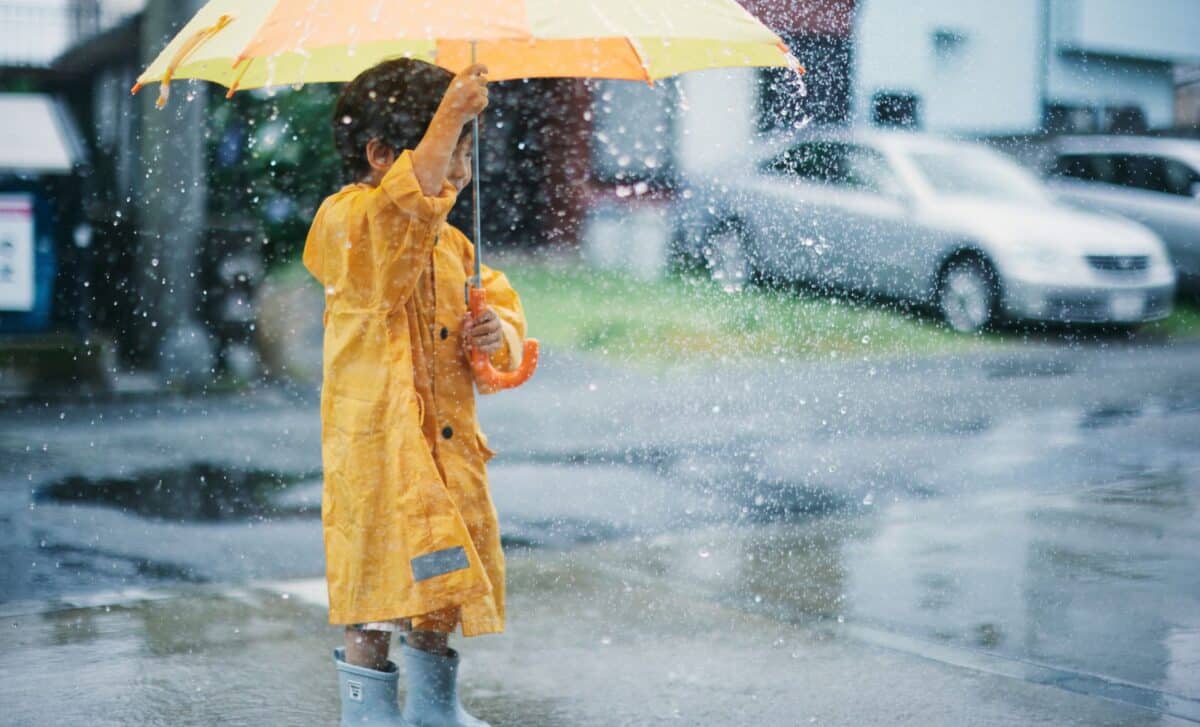 Enfant en imperméable jaune jouant sous la pluie