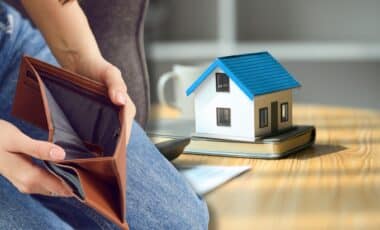 Une femme tient un portefeuille vide et un prototype de maison sur la table