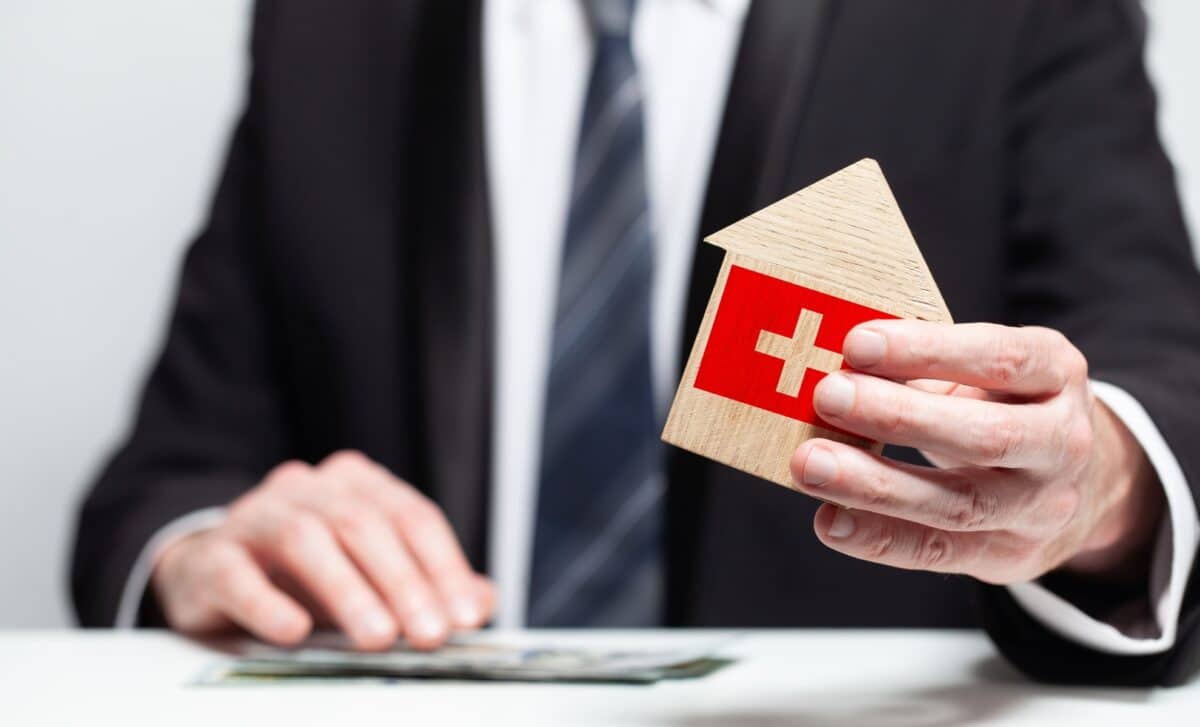 Homme tenant une maquette de maison en bois avec drapeau suisse.