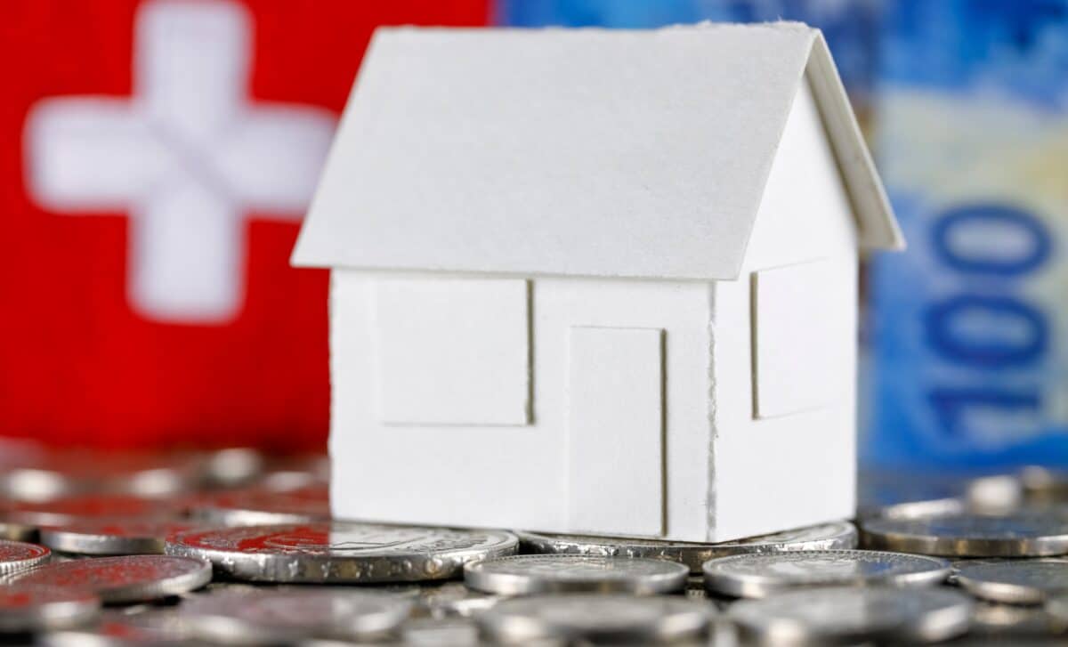 Modèle d'une maison sur fond de billets en francs suisses, de pièces de monnaie et du drapeau suisse