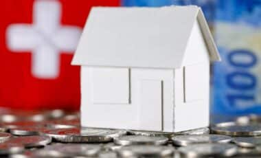 Modèle d'une maison sur fond de billets en francs suisses, de pièces de monnaie et du drapeau suisse