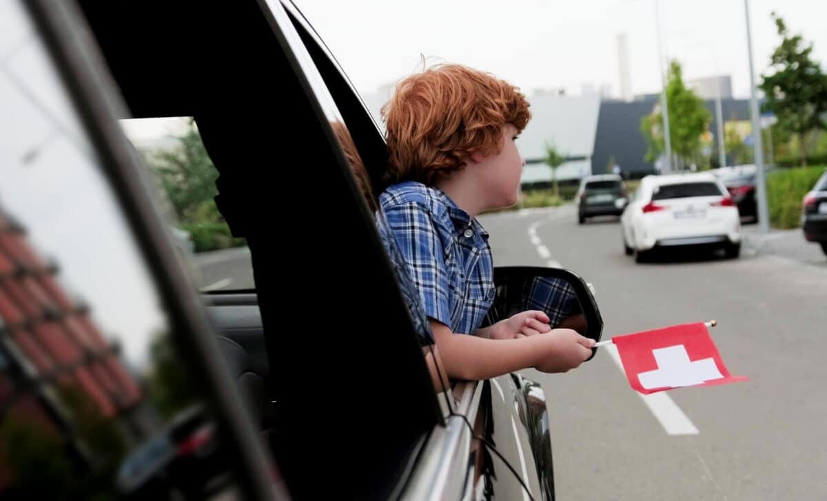 Garçon voyageant en voiture tenant le drapeau de la Suisse
