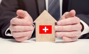 Homme tenant une maquette de maison en bois avec drapeau suisse