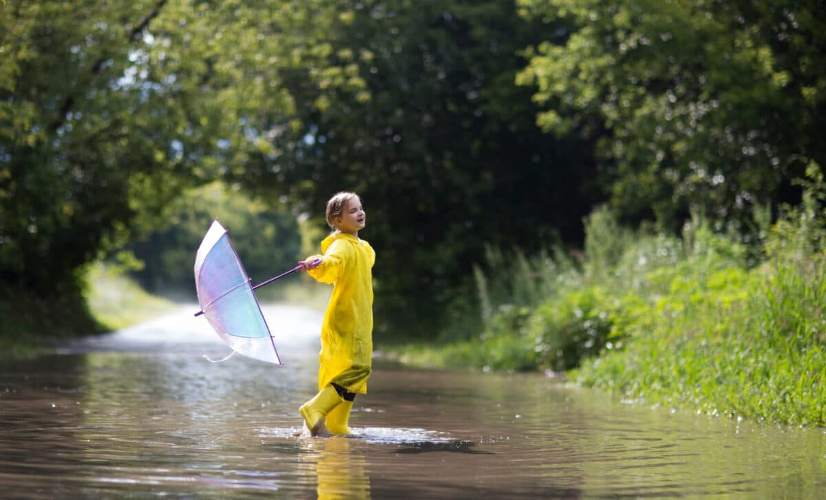 petite fille portant des bottes en caoutchouc et un imperméable jaunes avec un parapluie