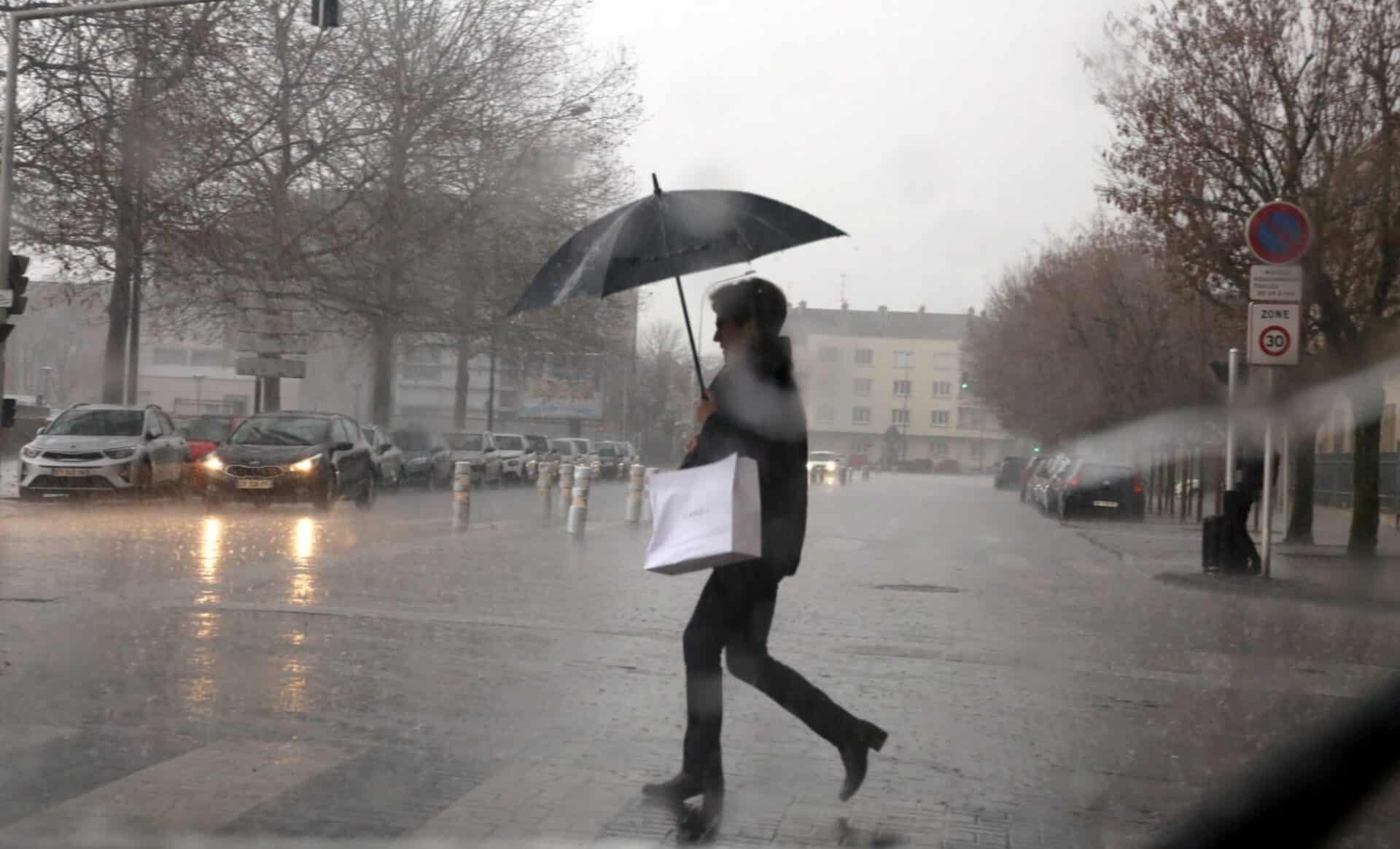 Une météo agitée illustrée par une photo d'une femme qui traverse la rue avec un parapluie