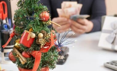 Photo de décorations de Noël posées sur un bureau, avec, en arrière-plan, une personne comptant des billets d'argent pour illustrer la prime de Noël