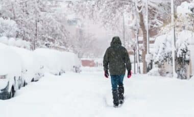 Photo montrant un piéton vêtu d'une veste à capuche noire dans une rue avec une couche importante de neige pour illustrer la perturbation météorologique qui s'apprête à s'abattre sur la France