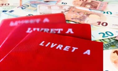 Trois carnets illustrant le Livret A posé sur une table où il y a des billets d'argent.