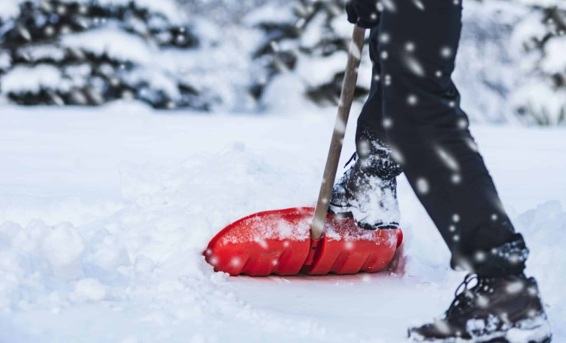 Personne se servant d'un râteau de neige sur une surface fortement enneigée. Photo utilisée pour illustrer la météo hivernale