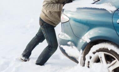 Un automobiliste qui pousse sa voiture bloquée par la neige