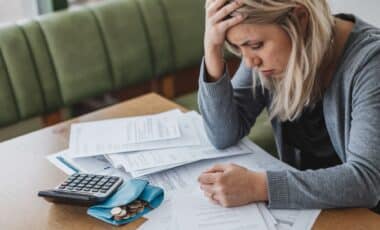 Une femme assise devant un bureau en bois avec des factures et une calculatrice pour évoquer les aides sociales