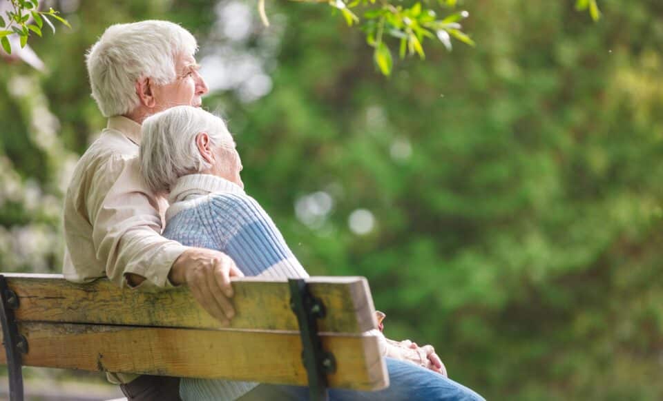 Cette image montre un couple de personnes âgées assis sur un banc dans un environnement verdoyant. Elle illustre un moment de sérénité et pourrait symboliser les bénéficiaires potentiels de l’Allocation de solidarité aux personnes âgées (Aspa), qui vise à assurer un minimum de revenus pour les retraités modestes.