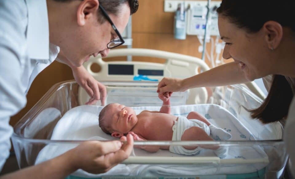 Un nouveau-né dans son berceau à l'hôpital, entouré de ses parents pour évoquer les Congés parentaux