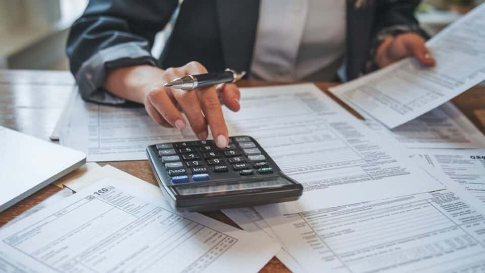 Une photo d'une personne qui fait des calculs avec une calculatrice sur un bureau plein de feuille pour évoquer l'indexation du barème des impôts