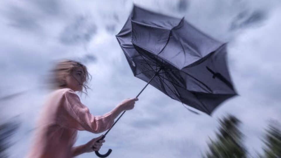 Une femme qui tient un parapluie et qui se renverse pour évoquer une météo venteuse