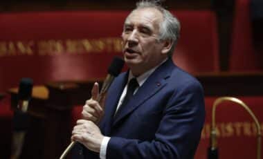 Cette image montre François Bayrou, le Premier ministre français, s'exprimant au micro dans un hémicycle. En costume sombre, il semble défendre une position ou expliquer un point politique important, illustrant son rôle actif dans les débats parlementaires.