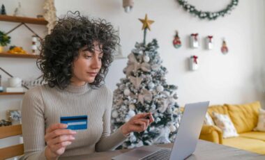 Une femme assise devant son ordinateur, une carte de crédit à la main avec un sapin en arrière-plan pour évoquer la fraude bancaire en période de fêtes