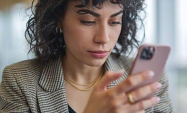 Une femme aux cheveux bouclés et vêtue d'un blazer utilisant un smartphone pour illustrer le Scam detection de Google contre les escroqueries téléphoniques