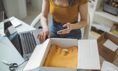 Une femme habillée d'un t-shirt orange et d'un jean en train de photographier un vêtement sur le point d'être emballé