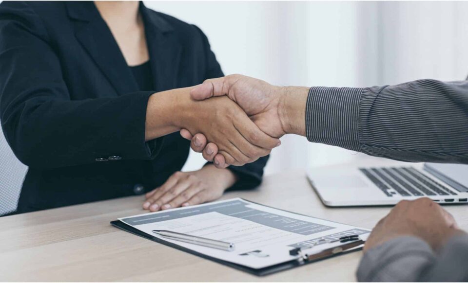 Deux personnes qui se serrent la main par-dessus un bureau en bois pour illustrer les métiers qui recrutent