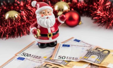 Une figurine du père Noël sur une table devant des billets de 50 euros, avec des décorations festives en arrière-plan pour illustrer la prime de Noël