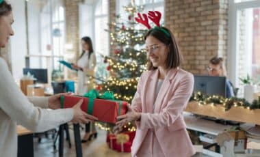 une femme vetue d'un blazer rose qui recoit un cadeau de Noel pour illustrer la prime de Noël