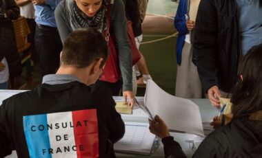 Un homme avec un t-shirt floqué 'Consulat de France" accueillant des expatriés