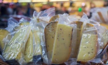 Cette image montre des portions de fromage emballées sous plastique, exposées dans un environnement commercial. Elle illustre le type de produits concernés par des rappels sanitaires, souvent dus à des contaminations bactériologiques, comme celles par la bactérie E.coli, nécessitant une vigilance accrue des consommateurs.