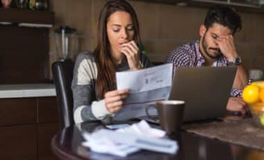 Cette image montre un couple visiblement préoccupé, examinant des factures à domicile. Elle illustre les difficultés financières auxquelles de nombreux ménages peuvent être confrontés, notamment dans le contexte des HLM,