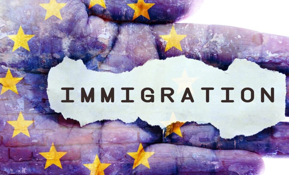 Cette image illustre le mot "Immigration" écrit sur un fond texturé, surimposé à une main et au drapeau de l'Union européenne. Elle symbolise le lien entre l'immigration et les politiques européennes, mettant en évidence les débats et enjeux liés à ce sujet dans le contexte actuel.