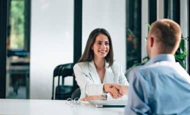 L'image montre une femme souriante en pleine discussion avec un homme, lors d'un entretien professionnel. Elle lui serre la main, symbolisant une étape clé dans le cadre d'un métier, potentiellement un entretien d'embauche ou une négociation.