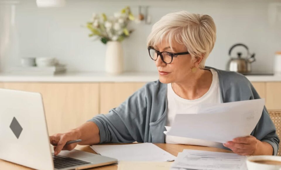 Une bénéficiaire de la pension de réversion tenant un document et regardant un ordinateur