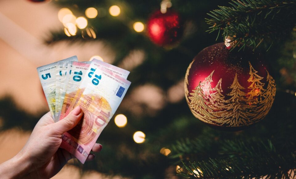 Un sapin de Noël avec une main tenant des billets d'argent pour illustrer la prime de Noël