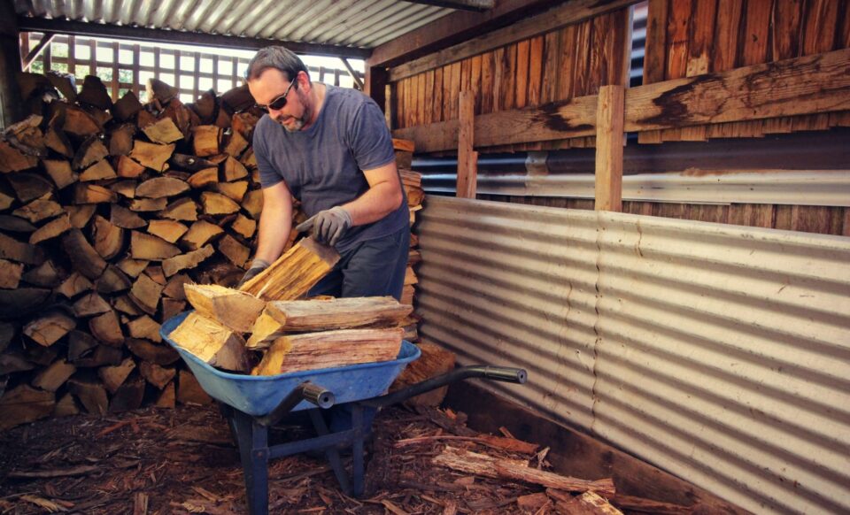 Un homme qui remplit une brouette de buches de bois de chauffage