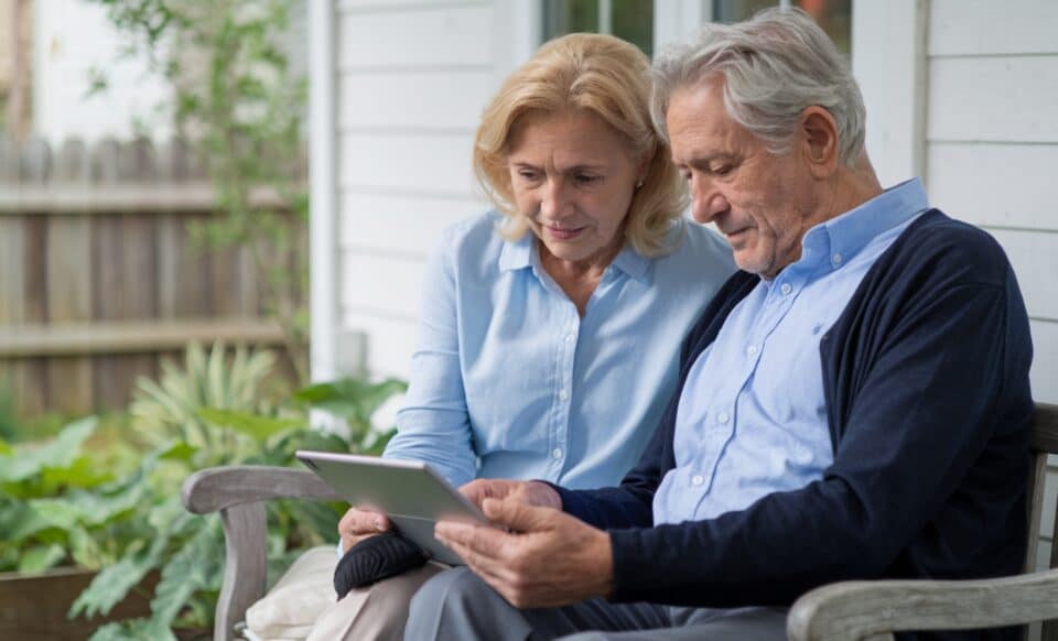 Un couple de retraités assis sur un banc, consultant une tablette.