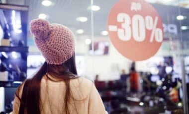 une personne portant un bonnet dans un magasin om on aperçoit une pancarte sur laquelle est écrit -30% pour symboliser la période de soldes d'hiver.