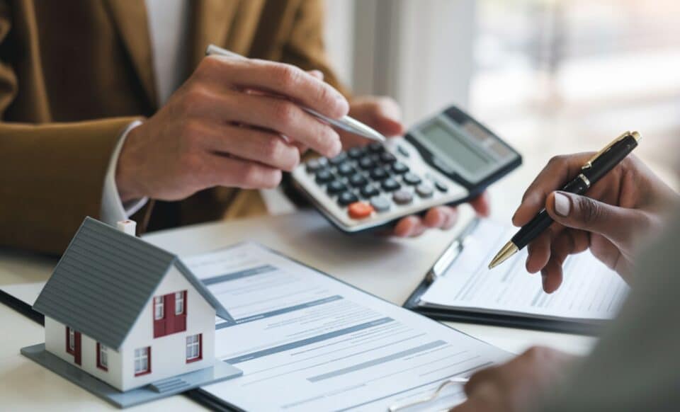 Deux personnes au cours d'une discussion, avec des stylos à la main et une maison miniature sur le bureau pour évoquer le crédit immobilier