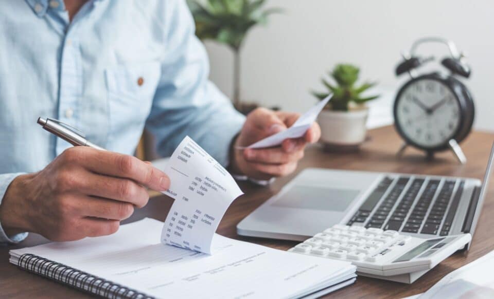 un homme en chemise bleu face à un ordinateur qui consulte des documents