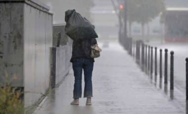 Une personne lutte contre des rafales de vent et de fortes pluies, illustrant des conditions météo extrêmes.