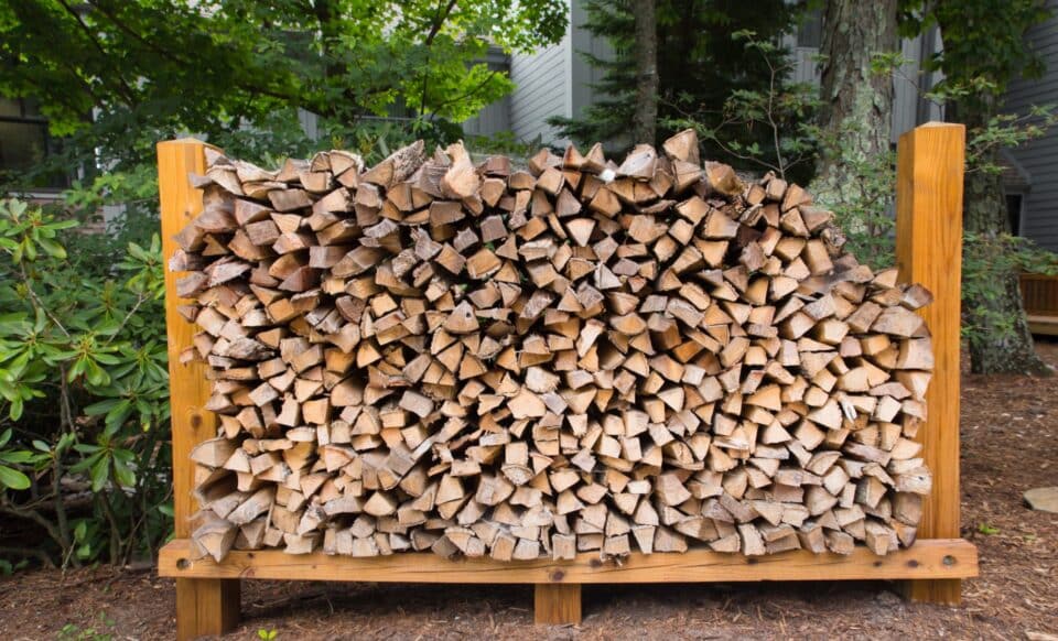 L'image montre un stock de bûches de bois de chauffage soigneusement empilé à l'extérieur, prêt pour une utilisation hivernale.