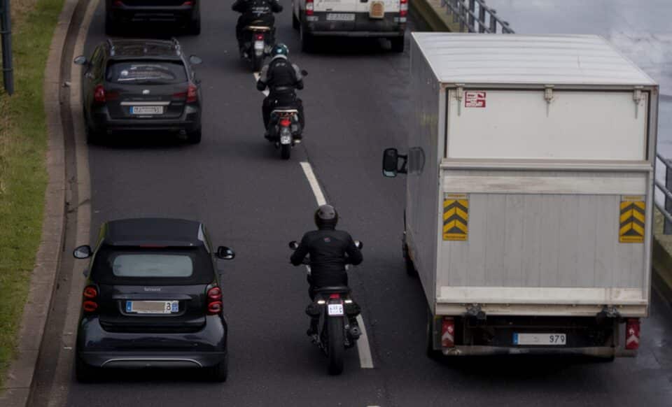 Cette image montre des motos circulant entre les files de voitures sur une route embouteillée, illustrant la pratique de la circulation inter-files.