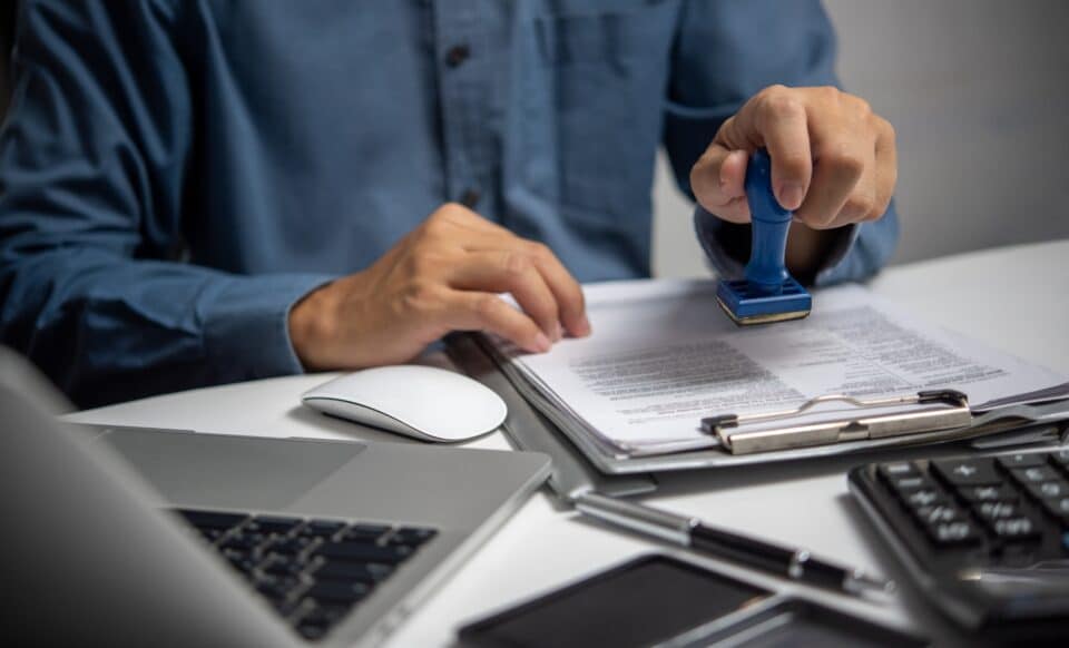 Cette image montre un agent administratif en train de tamponner des documents officiels, une activité courante dans le travail des fonctionnaires.