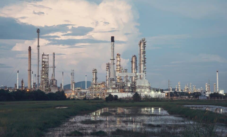 Raffinerie de gaz sous un ciel nuageux, entourée de végétation et de plans d'eau.