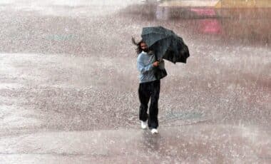 Une personne portant un parapluie marchant sous une pluie marquée par des vents forts et des chutes de pluie