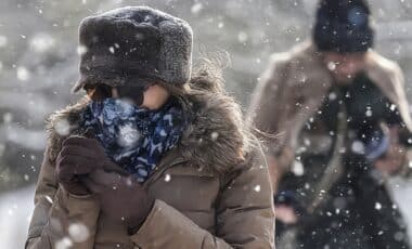 Une personne emmitouflée, protégée contre un froid intense, marche sous la neige, illustrant un épisode hivernal marqué par des conditions climatiques rigoureuses. Météo : vague de froid et intempéries.