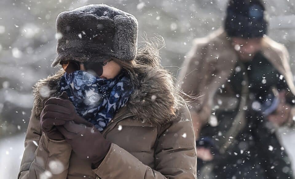 Une personne emmitouflée, protégée contre un froid intense, marche sous la neige, illustrant un épisode hivernal marqué par des conditions climatiques rigoureuses. Météo : vague de froid et intempéries.