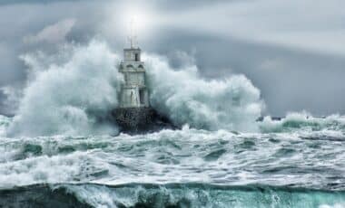 Un phare isolé est frappé de plein fouet par d'énormes vagues sous un ciel orageux, illustrant la puissance d'une tempête en mer.