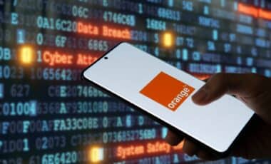 L’image montre un smartphone affichant le logo d’Orange, tenu par une main, sur un fond numérique avec des codes informatiques et des mots comme "Cyber Attack" et "Data Breach", suggérant une cyberattaque ciblant l’opérateur télécom.